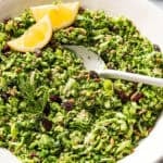 A spoon resting in a bowl of broccoli slaw garnished with lemon wedges.