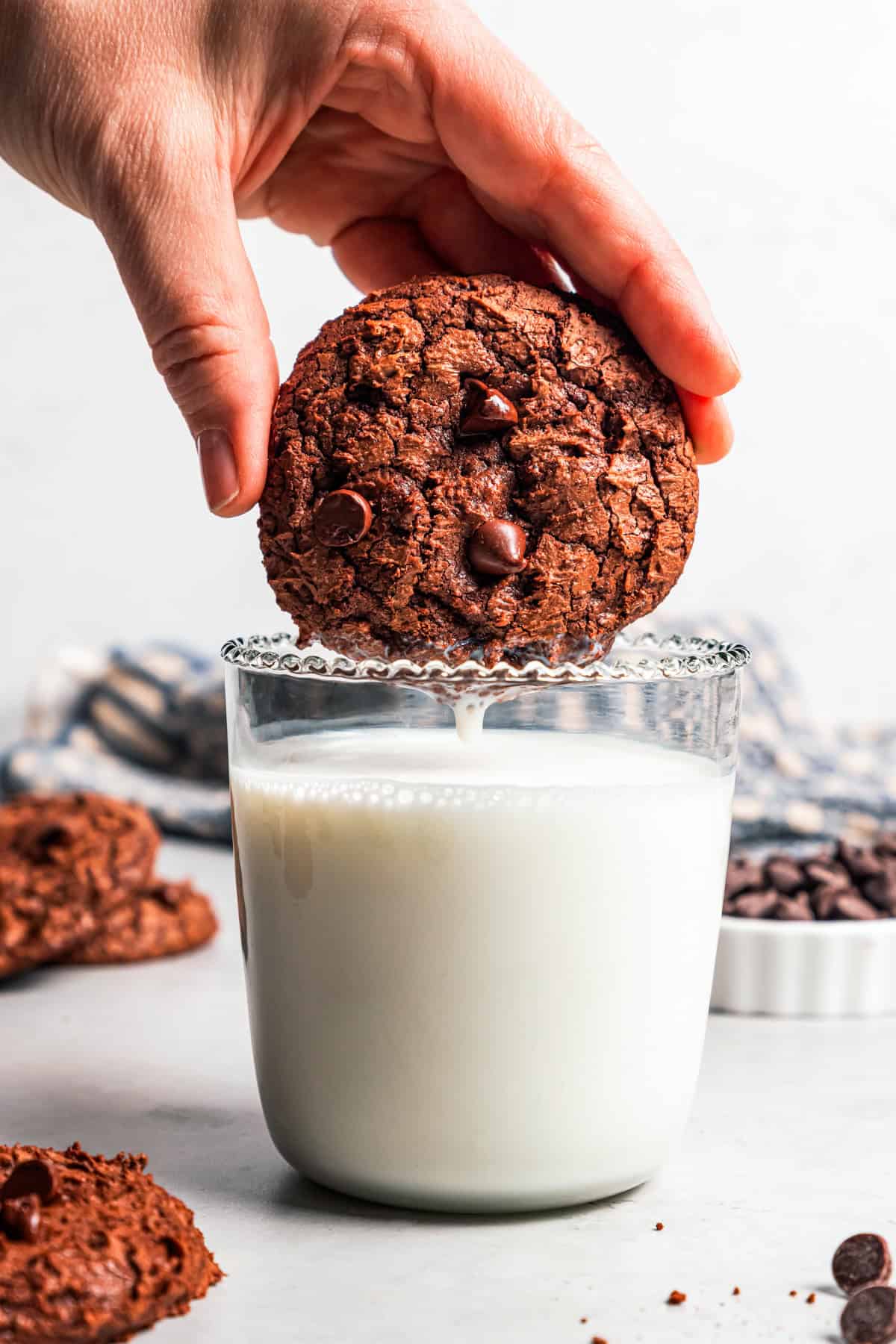 These chewy brownie cookies are the best of a fudgy brownie crossed with a soft-baked chocolate cookie! Made with real melted chocolate. A hand dunking a chewy brownie cookie into a glass of milk.