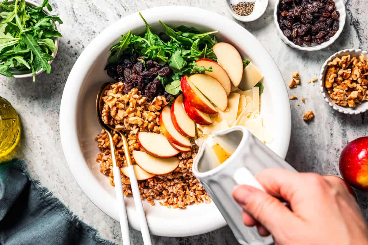 Pouring maple vinaigrette over a farro salad in a bowl.