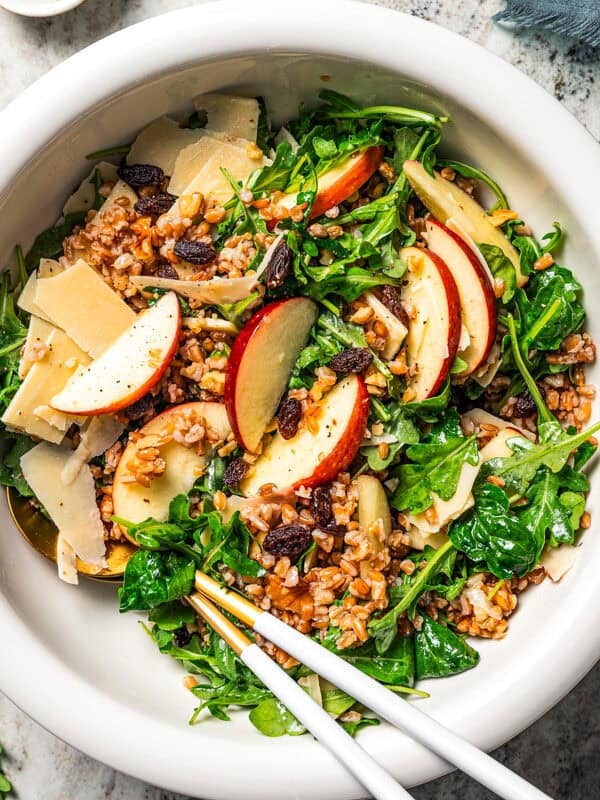 Overhead view of farro salad with arugula, apples, parmesan, walnuts, and maple vinaigrette served in a bowl.