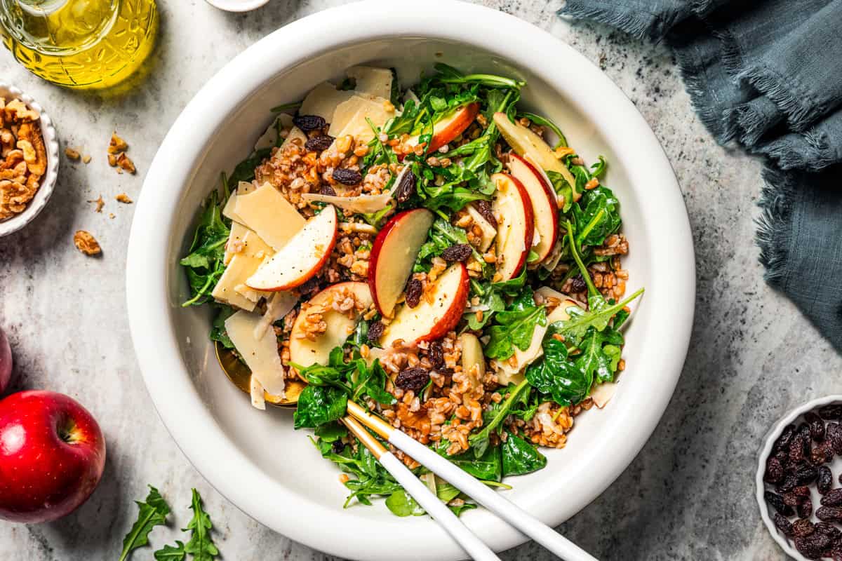 Overhead view of farro salad with arugula, apples, parmesan, walnuts, and maple vinaigrette served in a bowl.