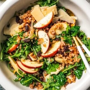 Farro salad with arugula, apples, parmesan, walnuts, and maple vinaigrette served in a bowl.