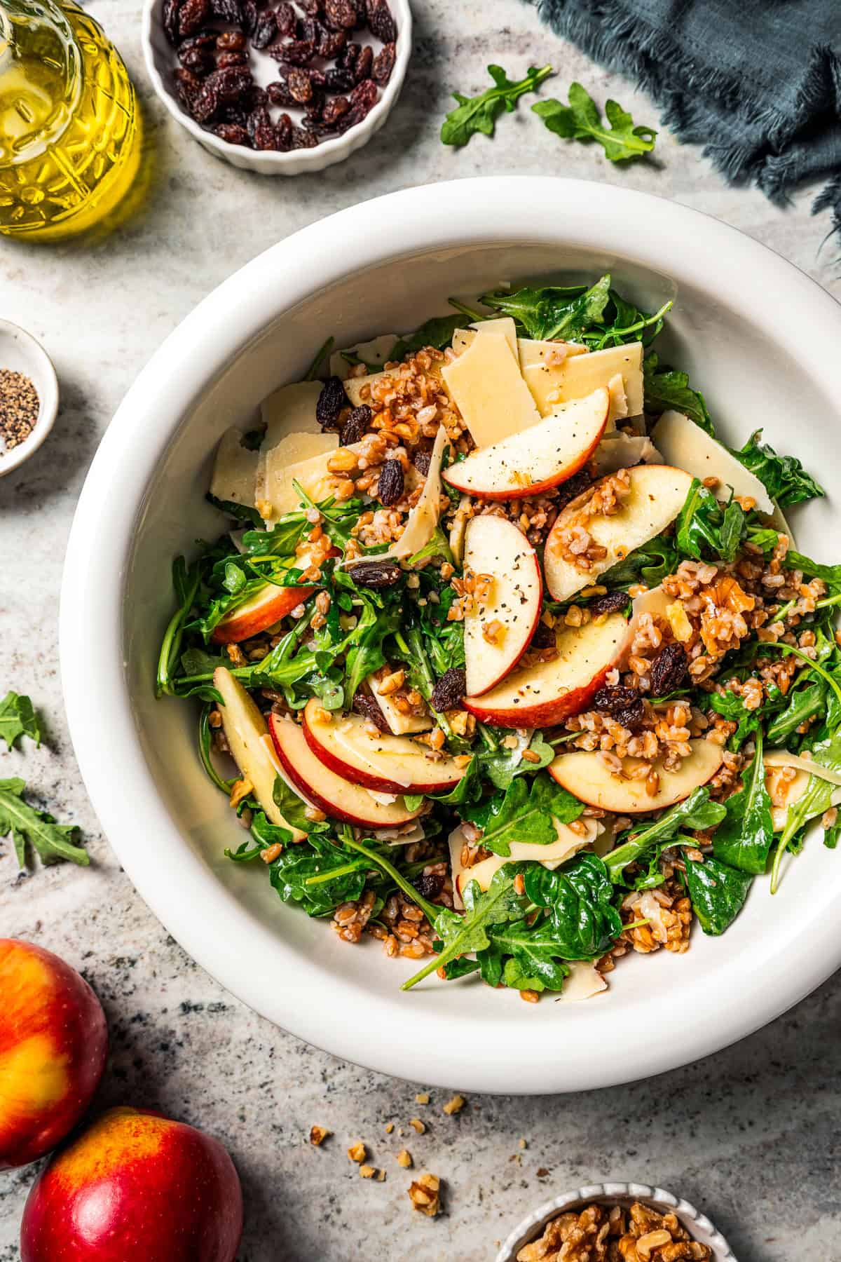 A bowl of farro salad with arugula, apples, parmesan, walnuts, and maple vinaigrette.