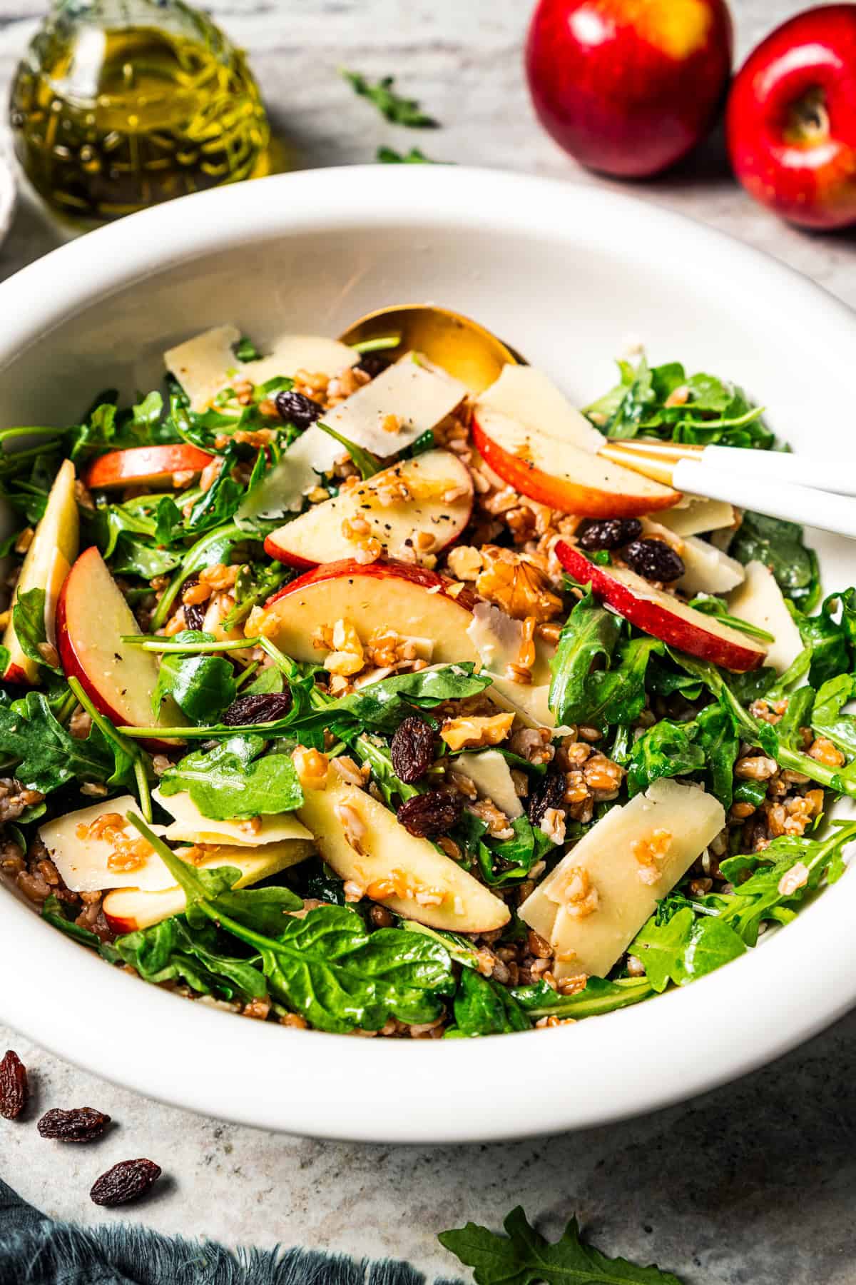 A bowl of farro salad with arugula, apples, parmesan, walnuts, and maple vinaigrette.