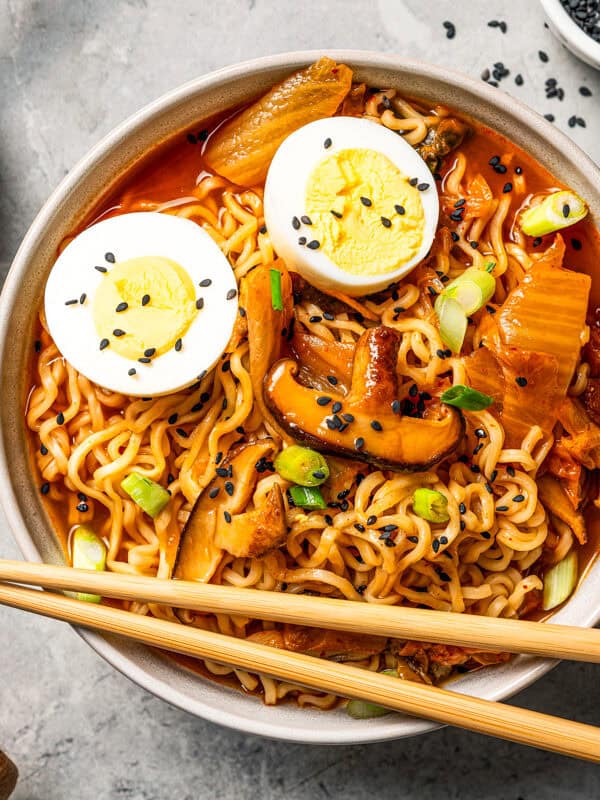 A bowl of spicy kimchi ramen with egg, mushrooms, and green onions, with chopsticks on the side.