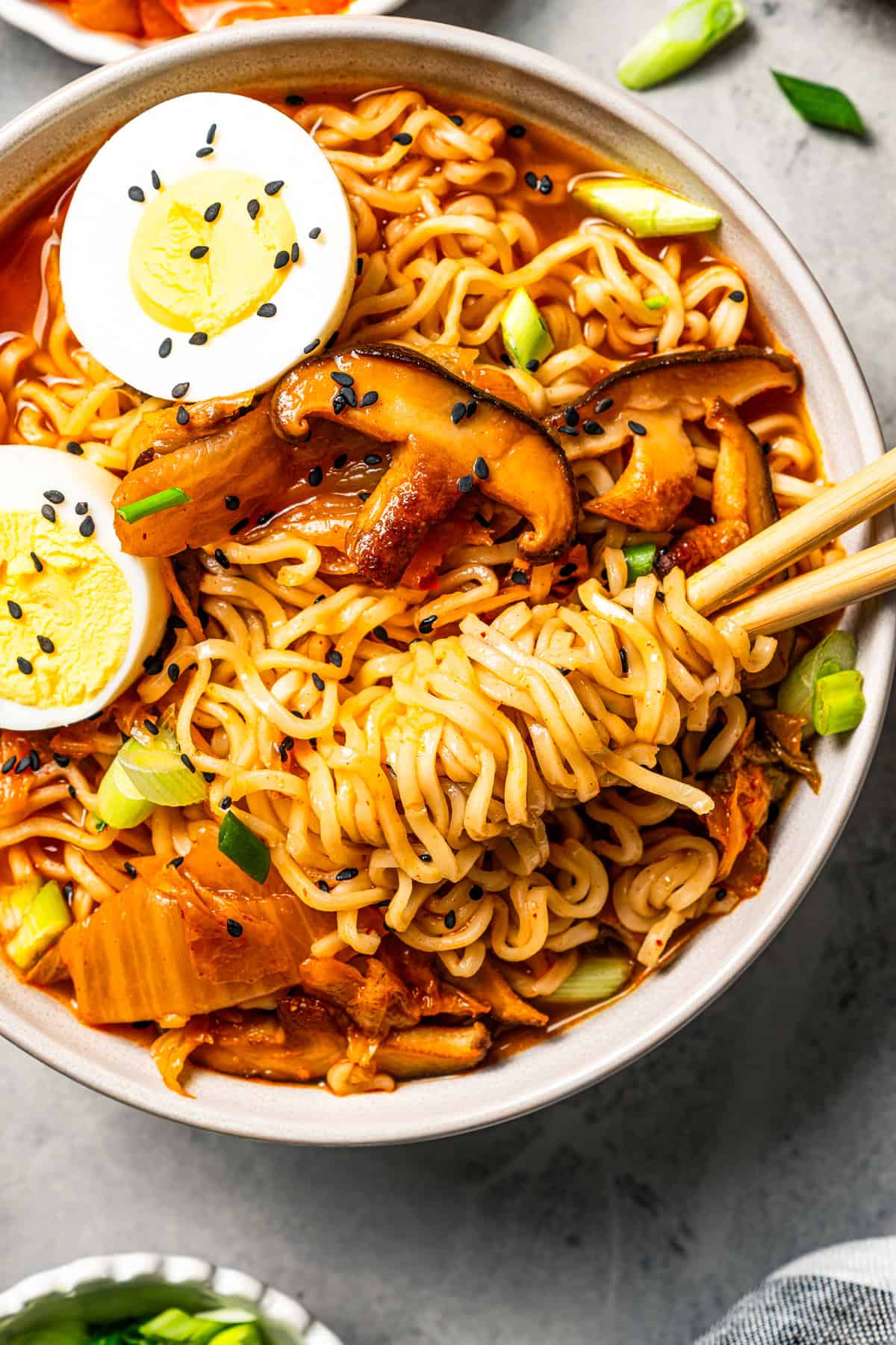 This quick and easy kimchi ramen recipe packs a spicy, savory punch with instant noodles, kimchi, shiitake mushrooms, and gochujang broth. Chopsticks rolled in noodles in a bowl of kimchi ramen.