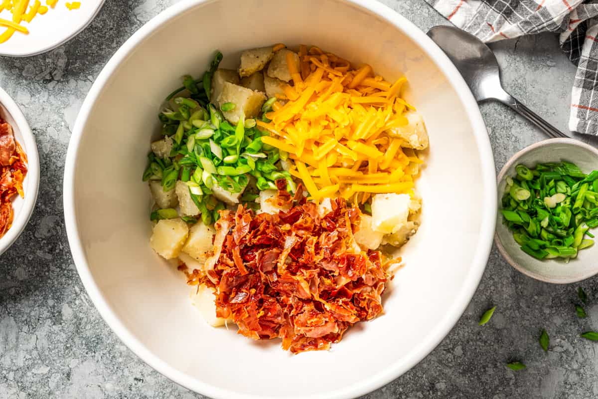 This rich and creamy loaded potato salad with bacon, spring onions, and cheddar cheese is easy to make ahead, perfect for potlucks and BBQs! A bowl of shredded cheddar cheese, diced potatoes, crumbled bacon, and green onions to make a potato salad.