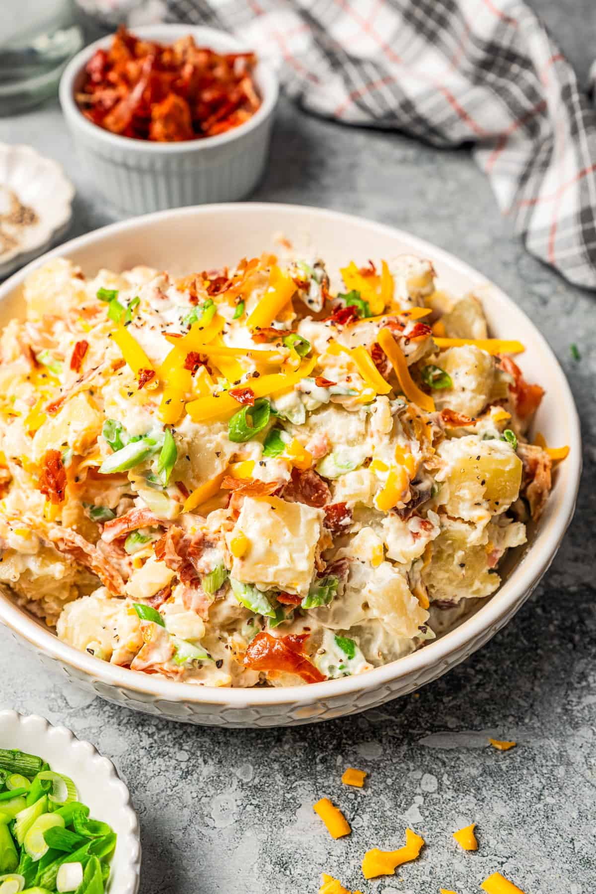 This rich and creamy loaded potato salad with bacon, spring onions, and cheddar cheese is easy to make ahead, perfect for potlucks and BBQs! A bowl of loaded baked potato salad with bacon and cheddar.