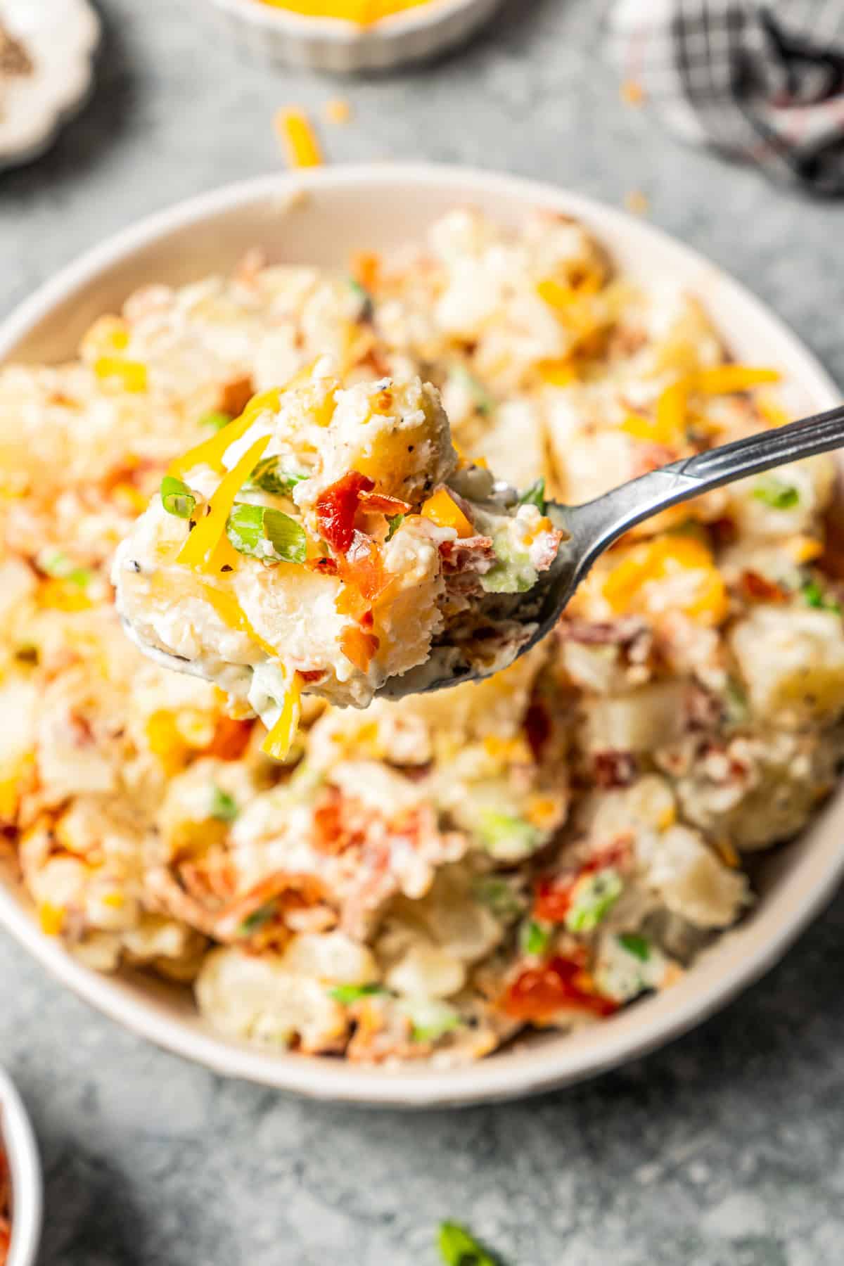 This rich and creamy loaded potato salad with bacon, spring onions, and cheddar cheese is easy to make ahead, perfect for potlucks and BBQs! A spoon holding up a spoonful of potato salad.