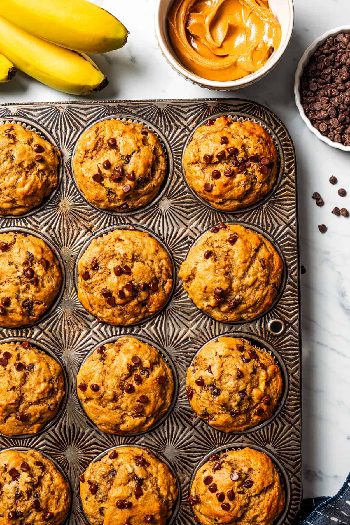 Peanut butter banana muffins are easy to make in one bowl! They’re super moist, with ripe bananas, creamy peanut butter, and chocolate chips. Freshly baked peanut butter banana muffins in a muffin pan.
