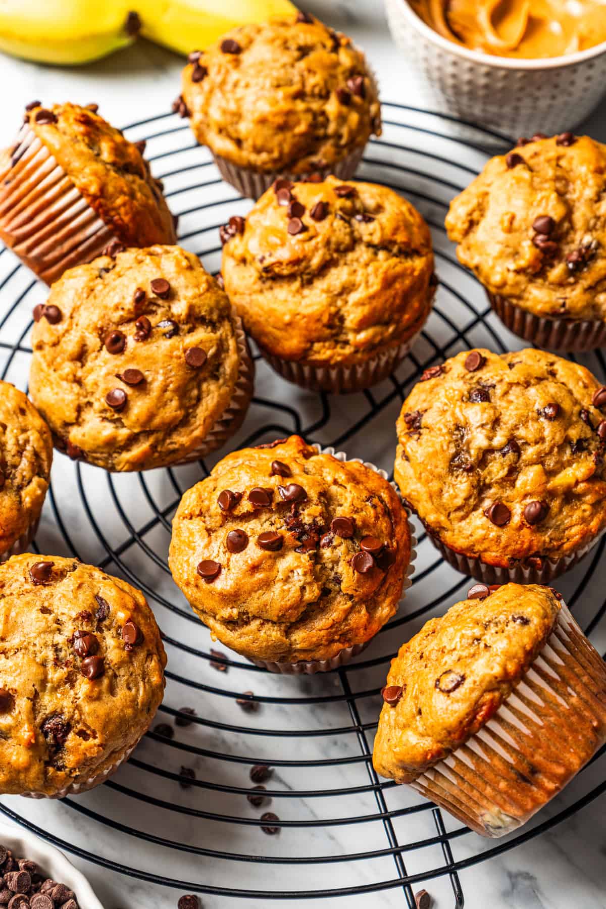 Peanut butter banana muffins are easy to make in one bowl! They’re super moist, with ripe bananas, creamy peanut butter, and chocolate chips. Peanut butter banana muffins studded with chocolate chips and arranged on a cooling rack.