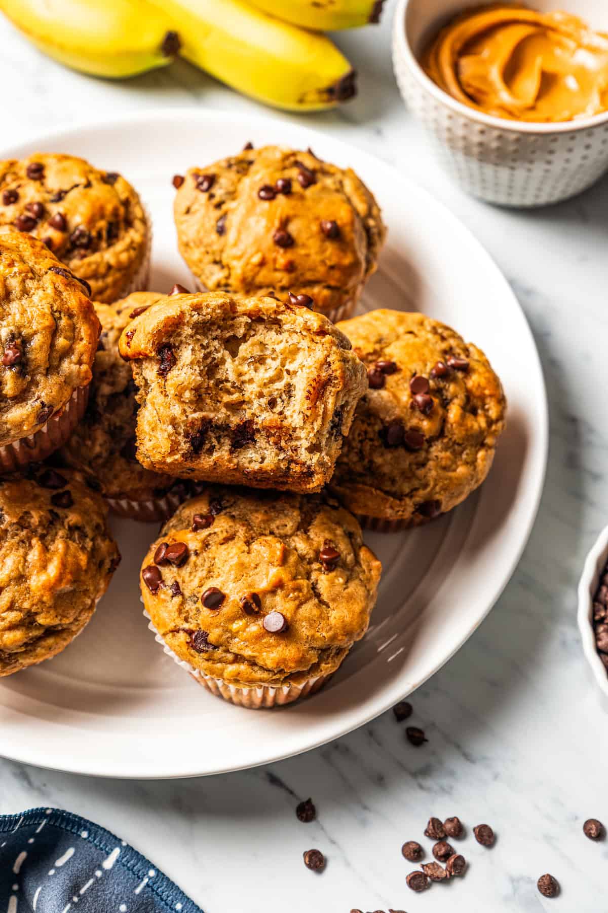 Peanut butter banana muffins are easy to make in one bowl! They’re super moist, with ripe bananas, creamy peanut butter, and chocolate chips. Peanut butter banana muffins stacked on a plate, with a bite missing from one muffin, revealing the chocolate chips inside.