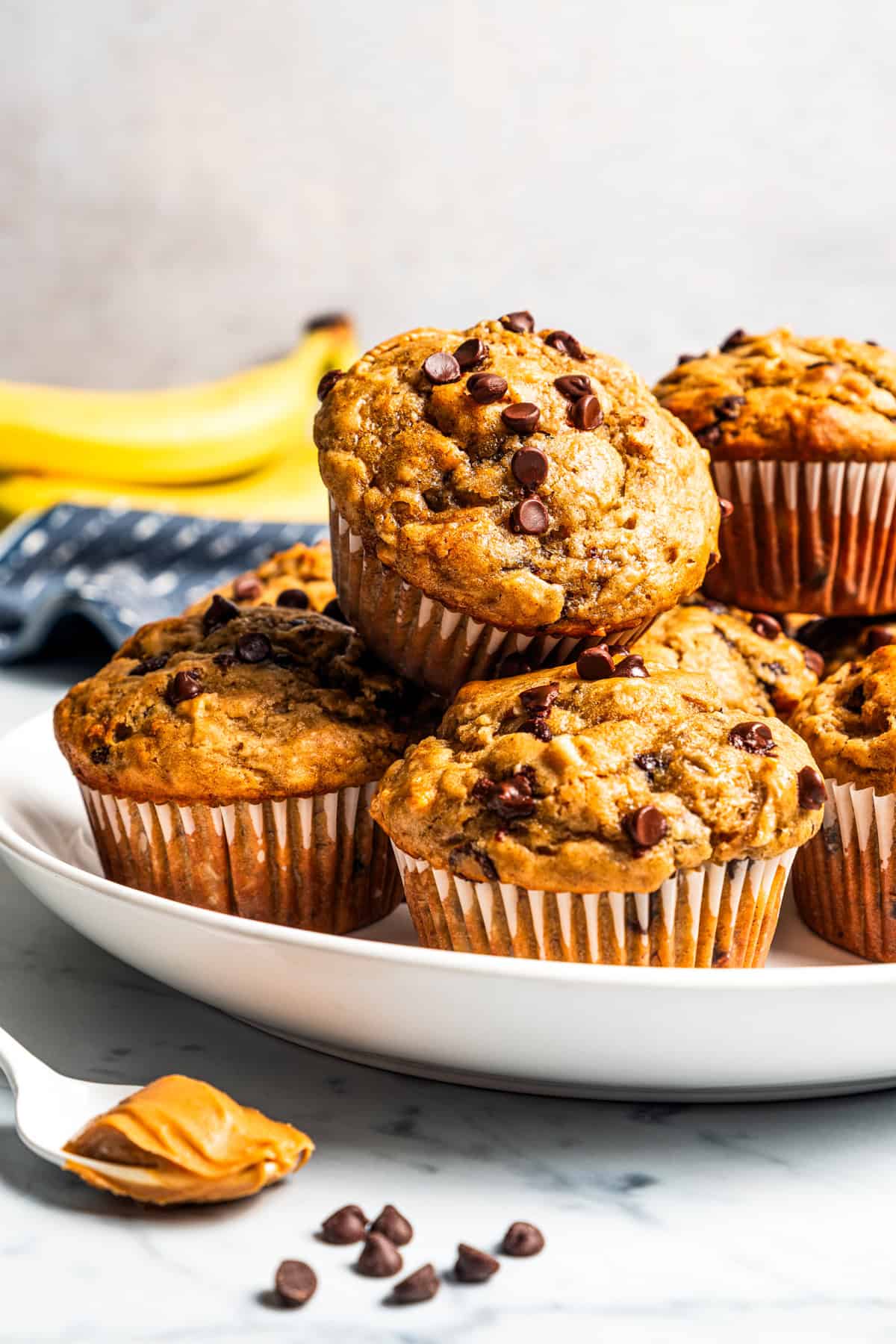 Peanut butter banana muffins are easy to make in one bowl! They’re super moist, with ripe bananas, creamy peanut butter, and chocolate chips. Moist, tender peanut butter banana muffins stacked on a plate.
