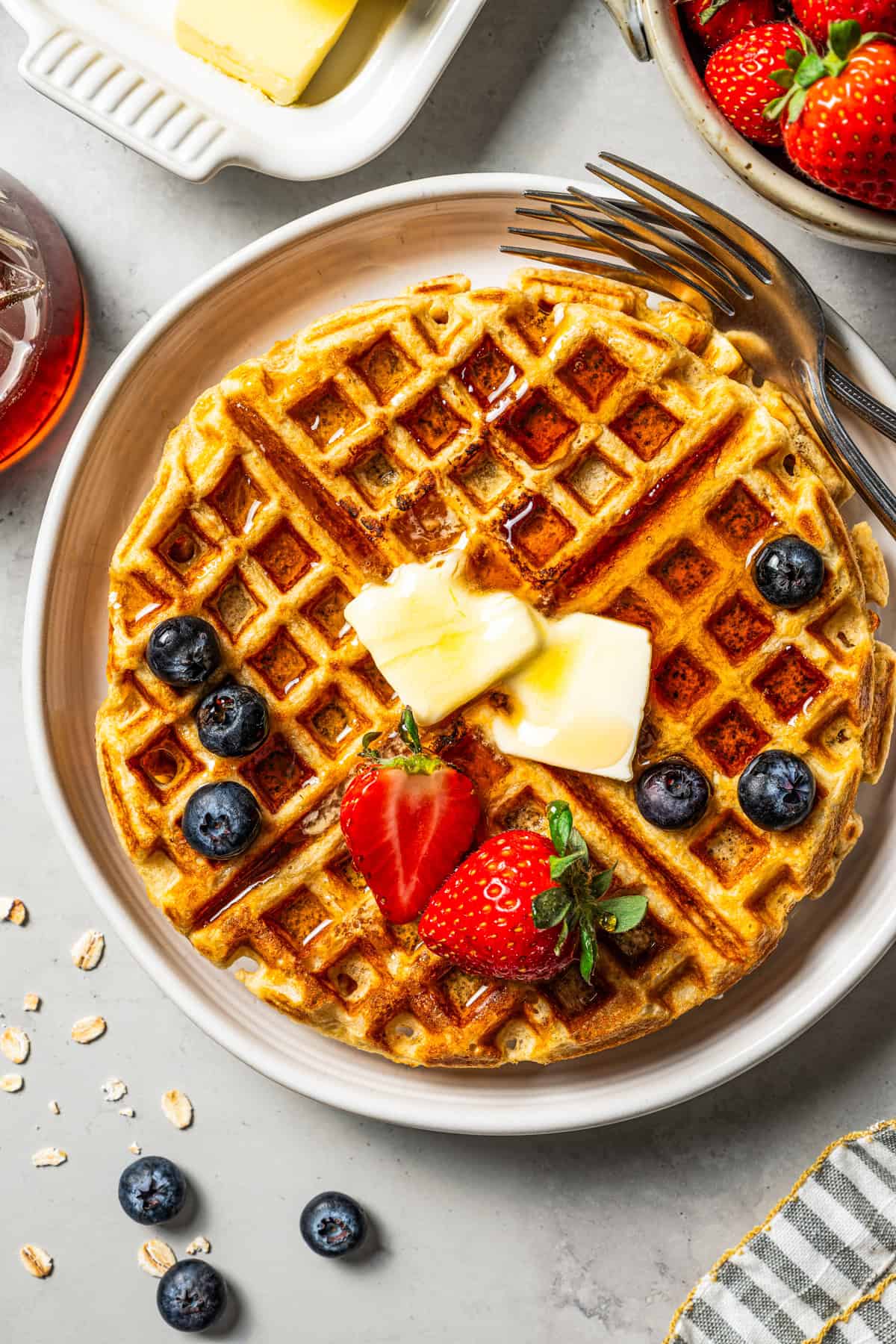 A protein waffle topped with fresh fruit, butter, and maple syrup on a plate.