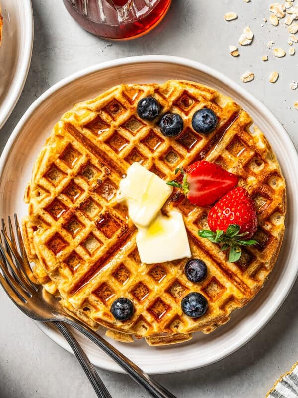 Two plates with waffles and a garnish of butter and berries. A bowl of strawberries is placed near the waffles.