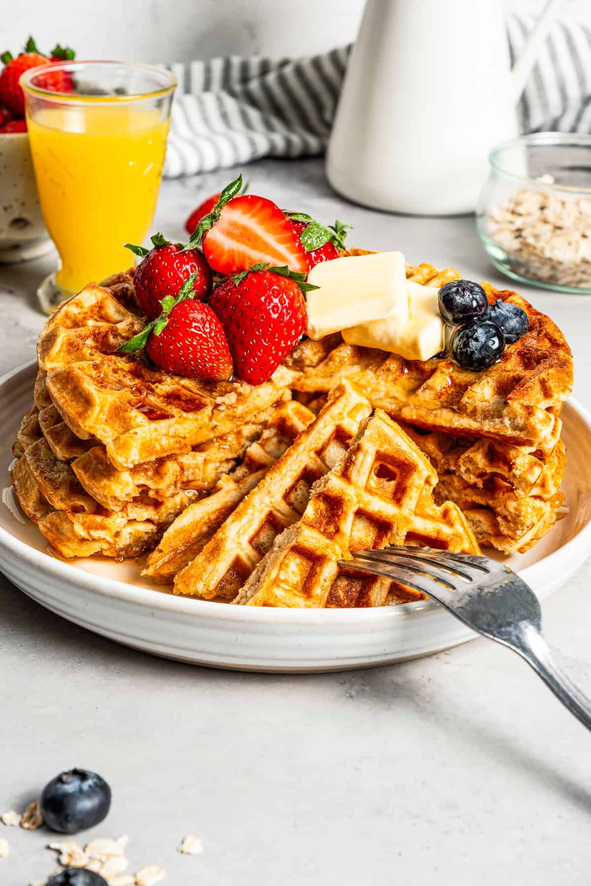 A stack of protein waffles topped with fresh fruit and butter, with a forkful cut from the stack.
