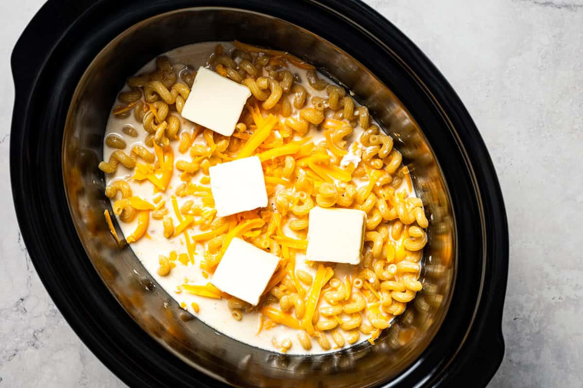 Ultra-creamy slow cooker mac and cheese is a dump-and-go version of my homemade mac and cheese recipe! Perfect for potlucks and holidays. Pats of butter are added to the pasta and cheese sauce ingredients inside a slow cooker.