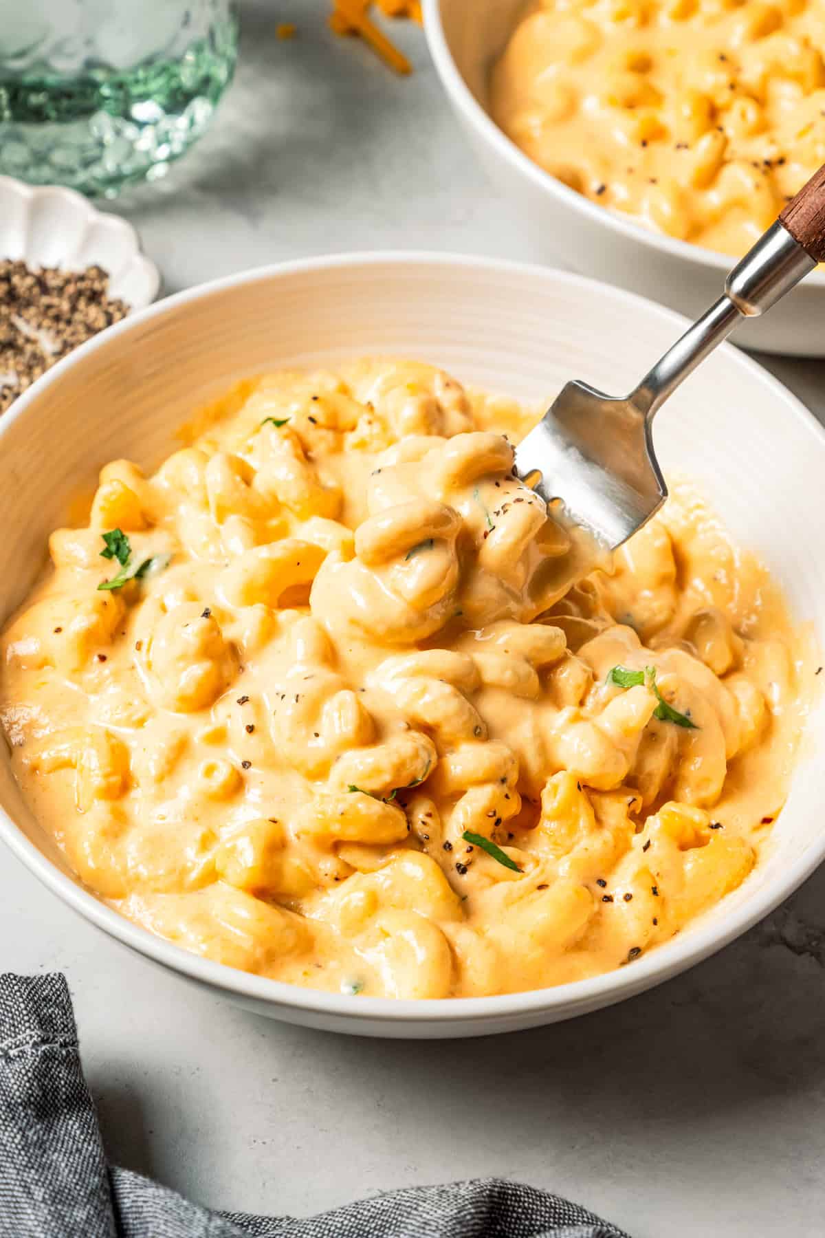 Ultra-creamy slow cooker mac and cheese is a dump-and-go version of my homemade mac and cheese recipe! Perfect for potlucks and holidays. Creamy slow cooker mac and cheese in a bowl with a fork twirling through.