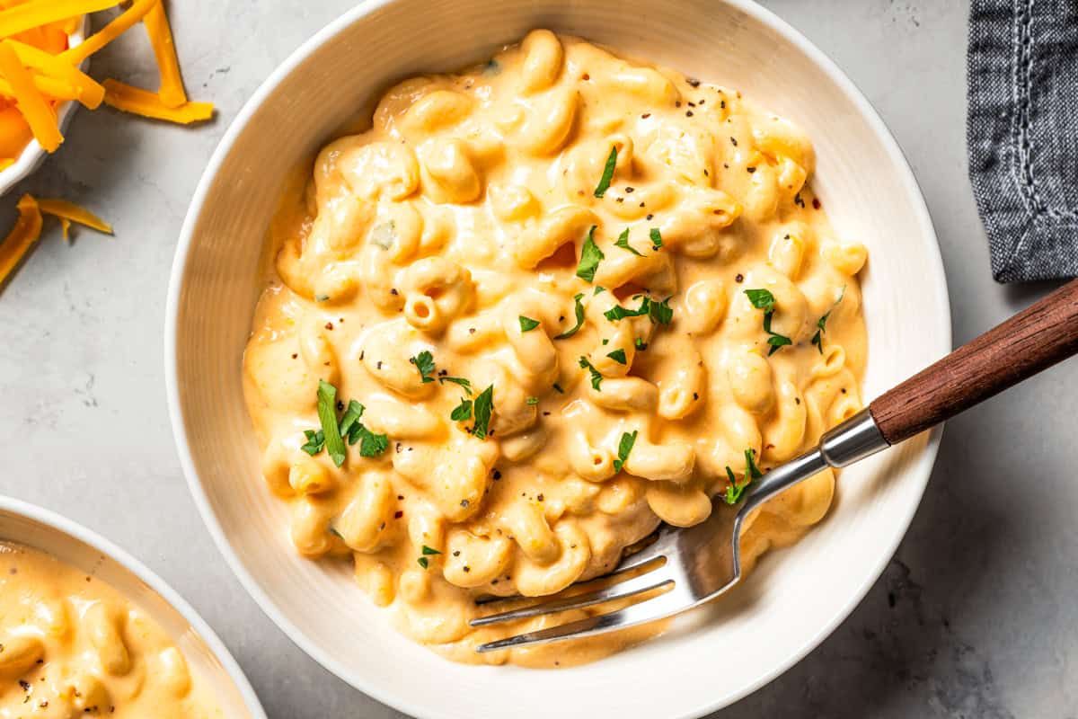 Ultra-creamy slow cooker mac and cheese is a dump-and-go version of my homemade mac and cheese recipe! Perfect for potlucks and holidays. Slow cooker mac and cheese in a bowl with a fork.