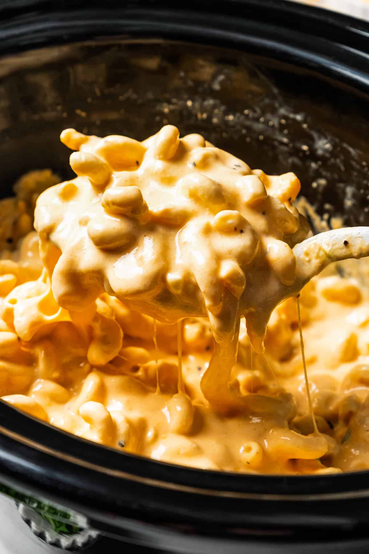 Ultra-creamy slow cooker mac and cheese is a dump-and-go version of my homemade mac and cheese recipe! Perfect for potlucks and holidays. A large serving spoon scooping homemade slow cooker macaroni and cheese.