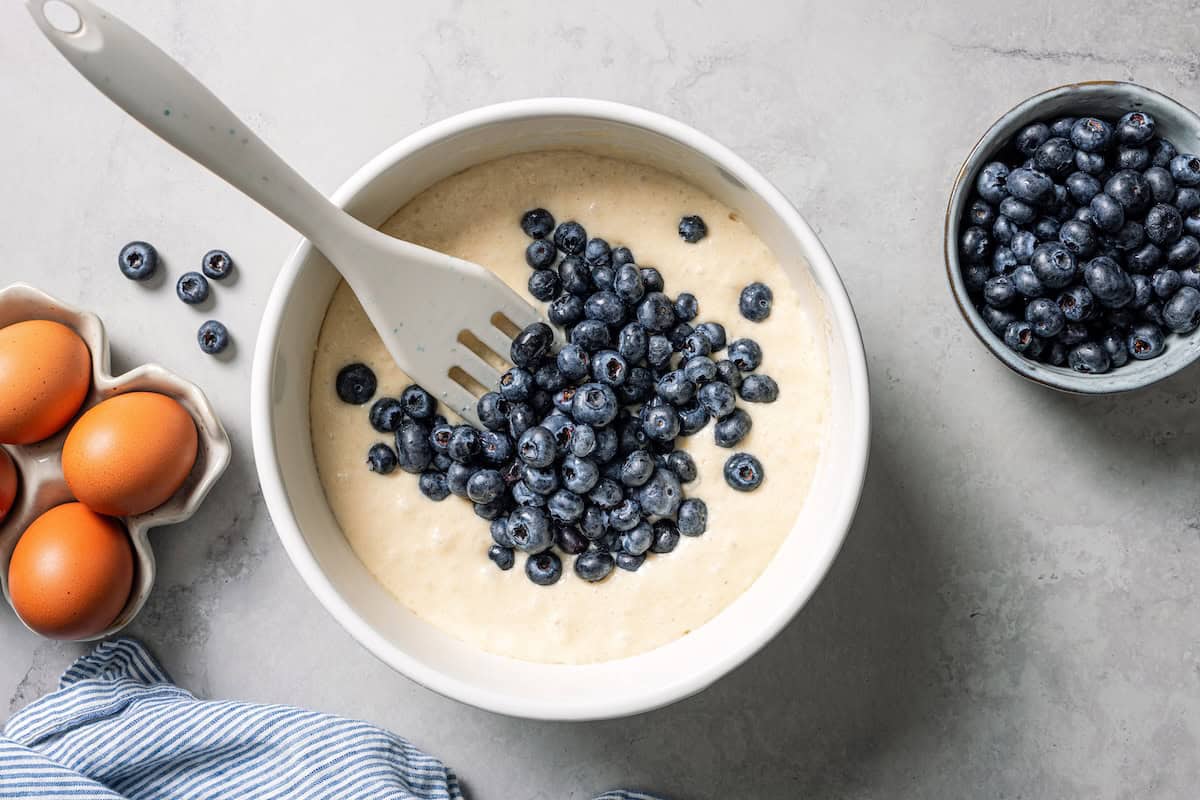 These classic blueberry waffles are light, fluffy, and ready in minutes. Rest the batter, then cook until they're golden brown and crisp. Folding fresh blueberries into rested waffle batter in a bowl.