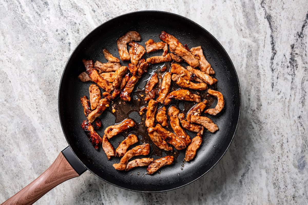 Craving moo shu pork for dinner? This homemade copycat is better than takeout and ready in 25 minutes with pork, veggies, and savory sauce. Fried moo shu pork strips in a skillet.