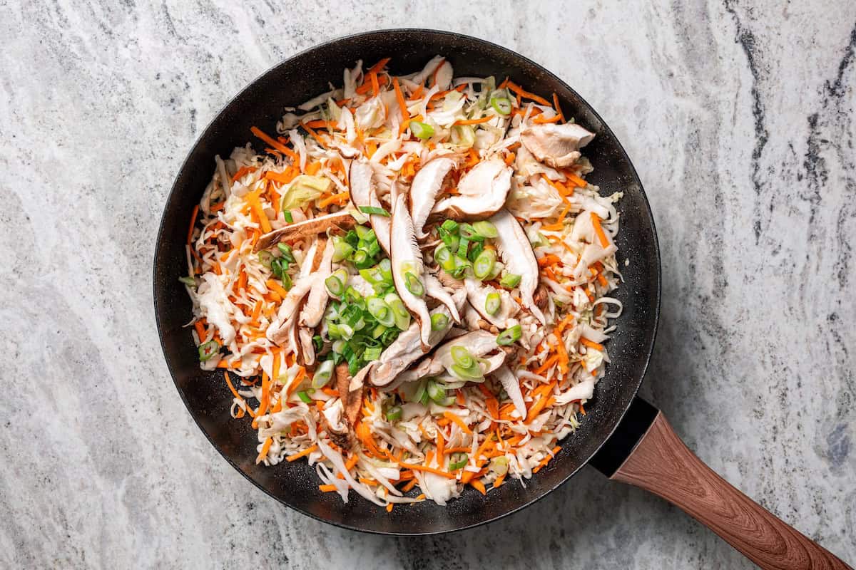 Craving moo shu pork for dinner? This homemade copycat is better than takeout and ready in 25 minutes with pork, veggies, and savory sauce. Coleslaw and veggies added to a skillet.