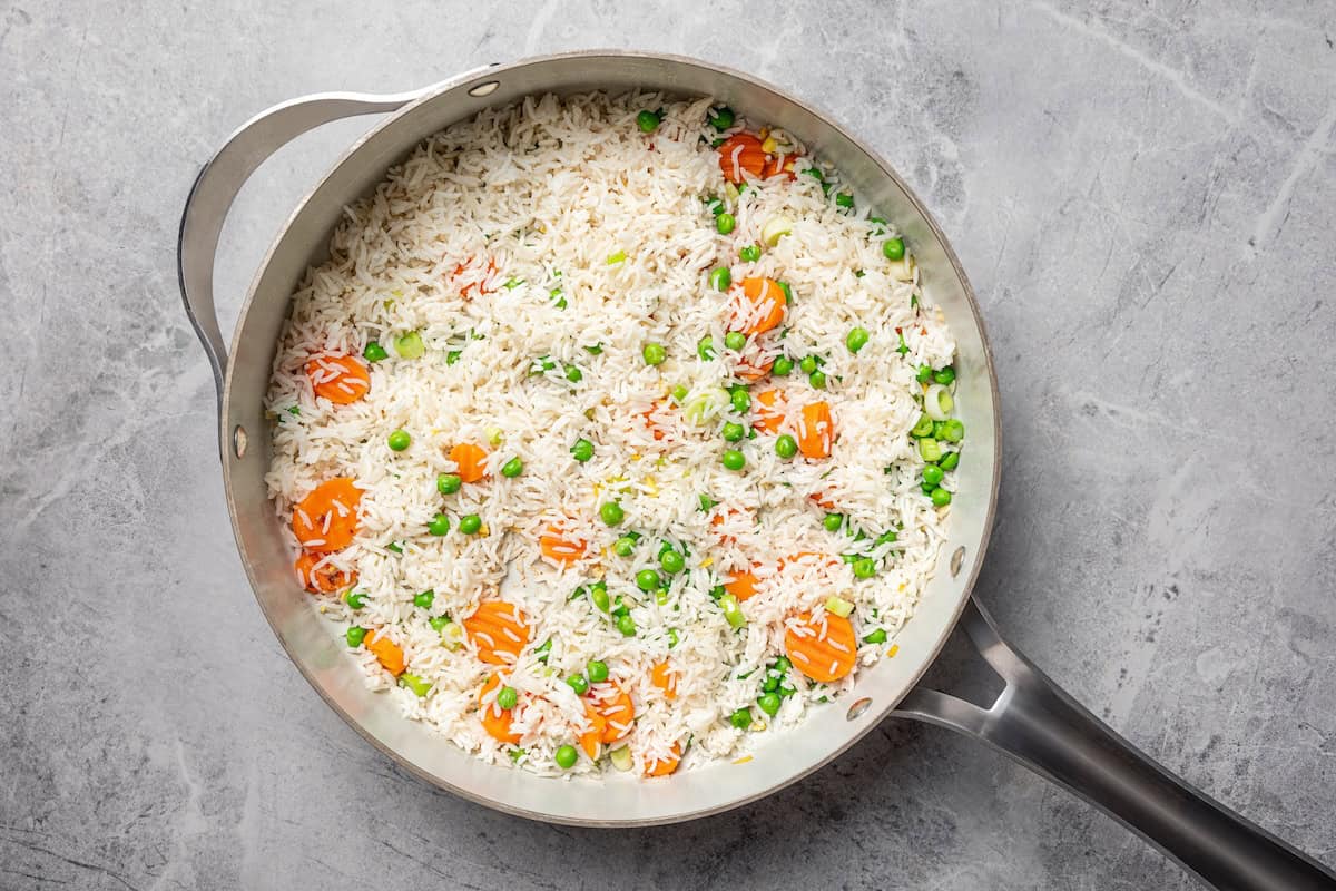 Pork fried rice is a quick, one-pan dinner packed with crispy ground pork, cooked eggs, and veggies. It's the best way to use up day-old rice! Cooked white rice added to vegetables in a skillet.