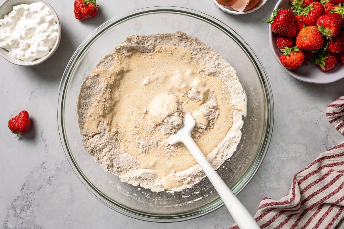 These moist strawberry protein muffins with applesauce, cottage cheese, and protein powder make an easy, light breakfast or meal prep snack! Folding together protein muffin batter in a bowl.