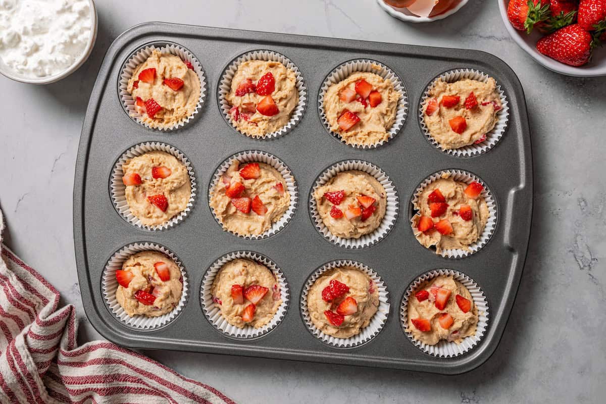 These moist strawberry protein muffins with applesauce, cottage cheese, and protein powder make an easy, light breakfast or meal prep snack! A lined muffin tin filled with strawberry protein muffin batter.