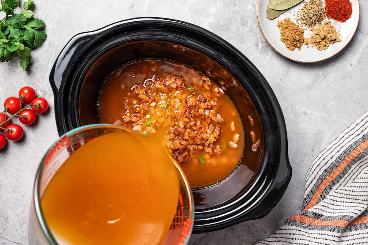 Slow cooker pinto beans are full of flavor and so easy to make. Add dry beans to the crock pot in the morning, and they’re tender by dinner! Pouring broth over pinto beans in the slow cooker.