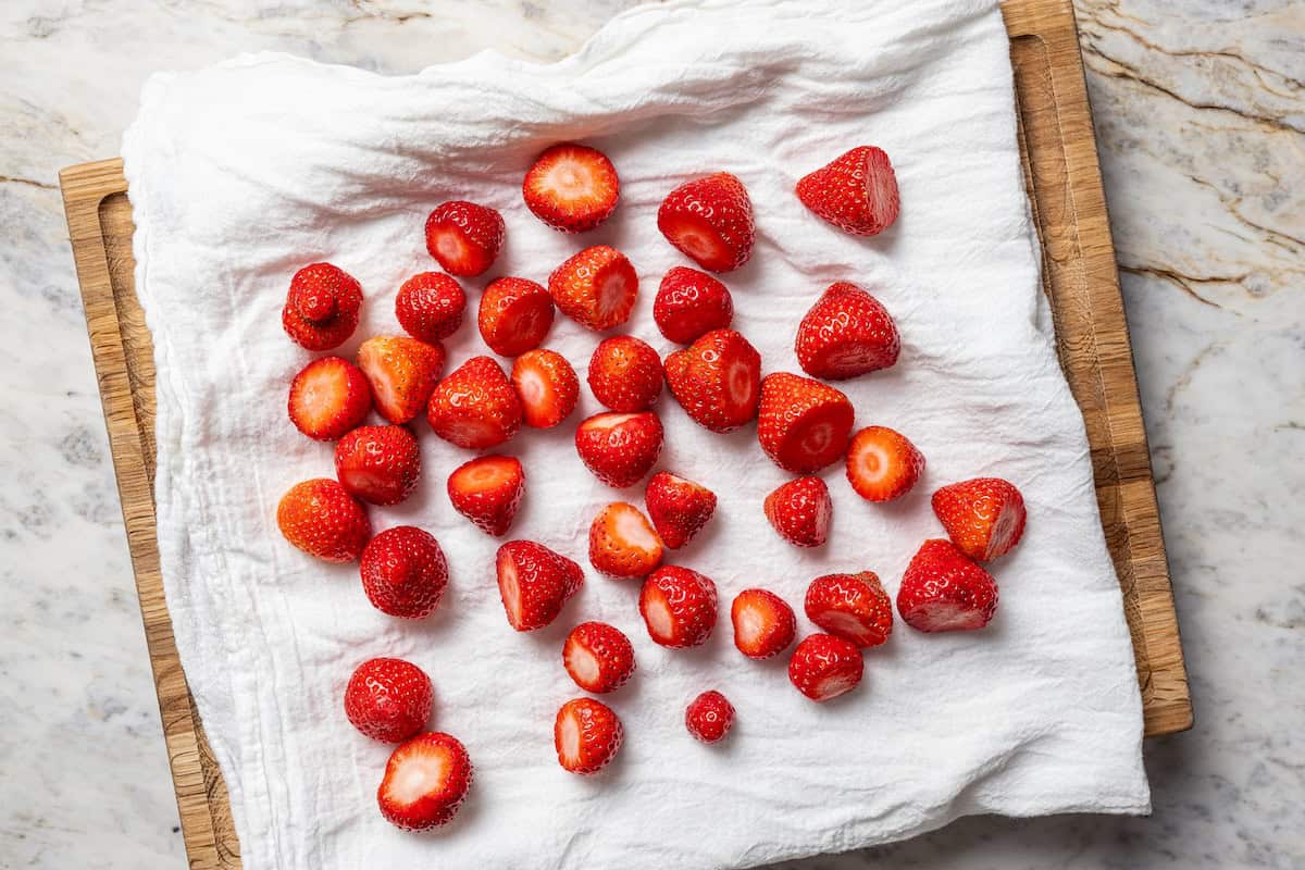 This no-bake strawberry icebox cake is an easy overnight dessert with layers of graham crackers, fresh strawberries, and fluffy whipped cream. Strawberries drying on a sheet of paper towel on top of a baking sheet.