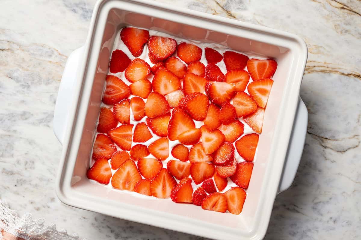 This no-bake strawberry icebox cake is an easy overnight dessert with layers of graham crackers, fresh strawberries, and fluffy whipped cream. Fresh strawberry slices layered over whipped cream in a baking dish.
