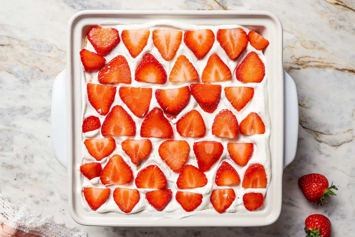 This no-bake strawberry icebox cake is an easy overnight dessert with layers of graham crackers, fresh strawberries, and fluffy whipped cream. Overhead view of strawberry icebox cake topped with fresh strawberry slices in a ceramic dish.