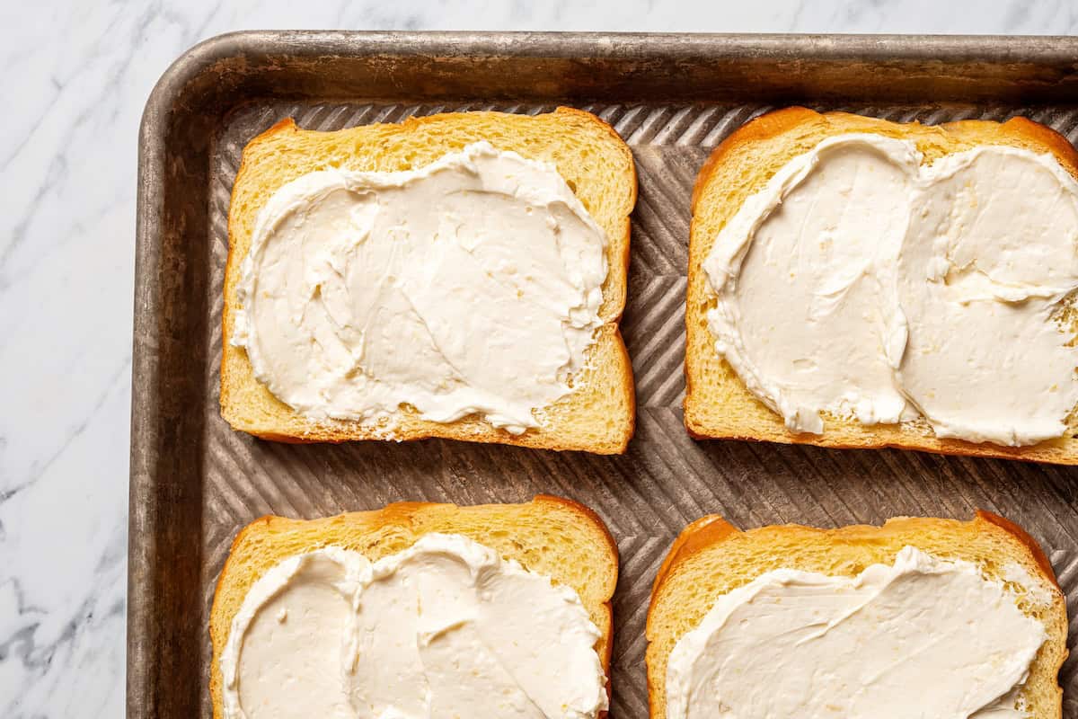 Make this cream cheese stuffed French toast with thick slices of custard-dipped brioche filled with sweet mascarpone and fresh lemon zest. Mascarpone cream cheese filling spread over bread slices on a baking sheet.