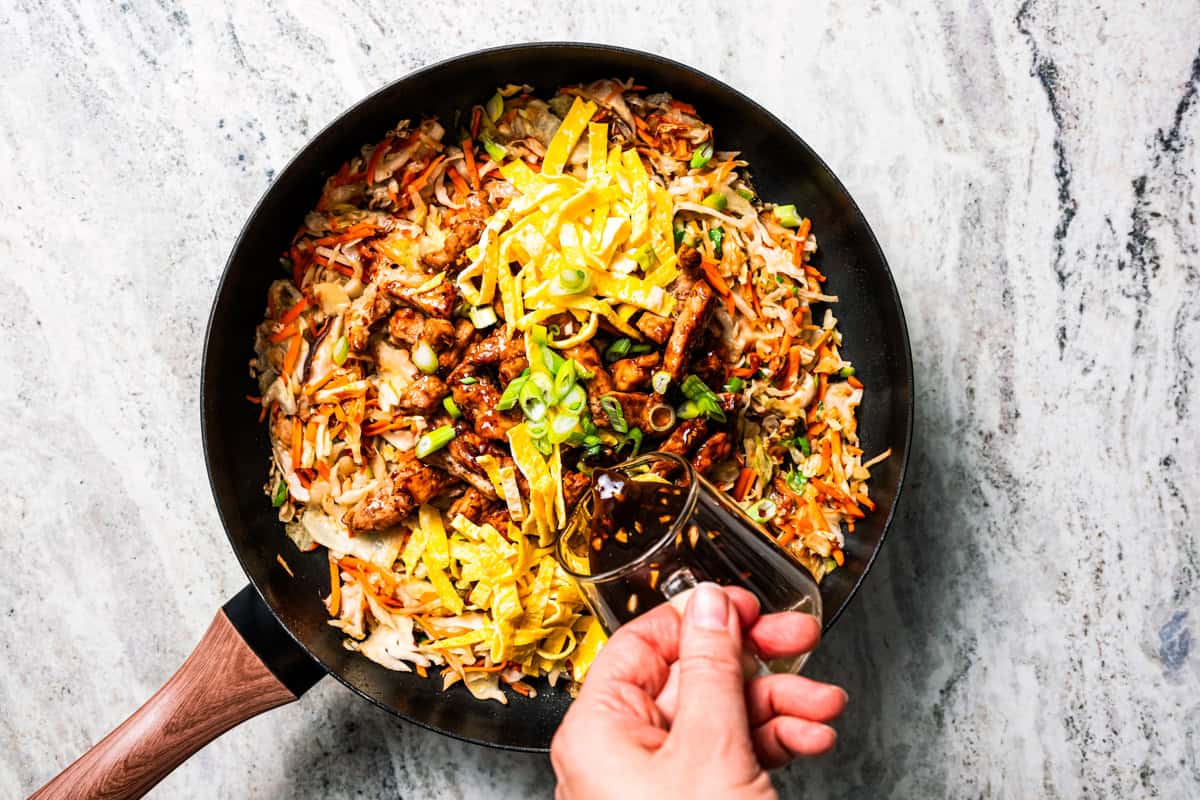 Craving moo shu pork for dinner? This homemade copycat is better than takeout and ready in 25 minutes with pork, veggies, and savory sauce. Pouring moo shu pork marinade over stir fry veggies and pork in a skillet.