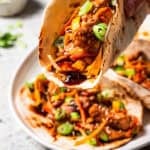 Close up of a hand holding a moo shu pork wrap with more wraps in the background.