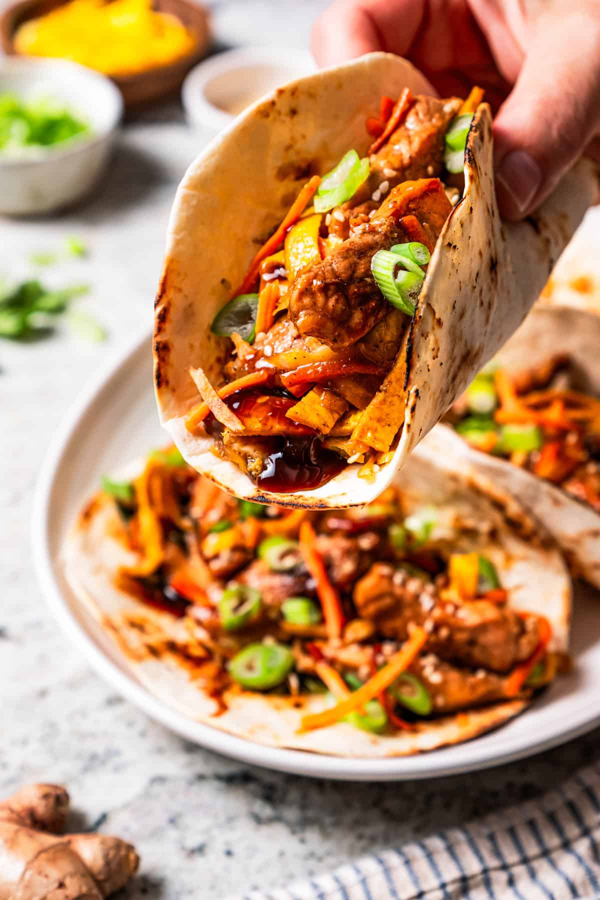 Craving moo shu pork for dinner? This homemade copycat is better than takeout and ready in 25 minutes with pork, veggies, and savory sauce. Close up of a hand holding a moo shu pork wrap with more wraps in the background.