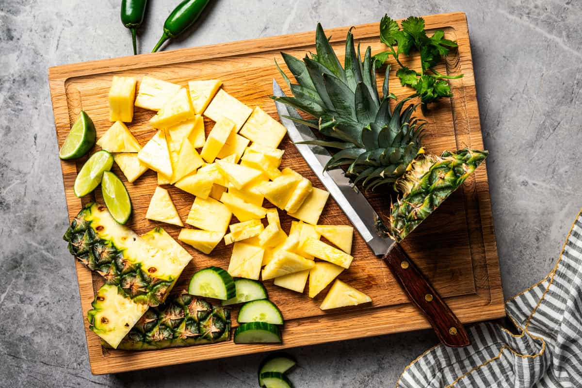 This refreshing pineapple cucumber salad is an easy side salad with fresh pineapple, crisp cucumber, spicy jalapeños, cilantro, and lime. Chopped pineapple on a wooden cutting board.
