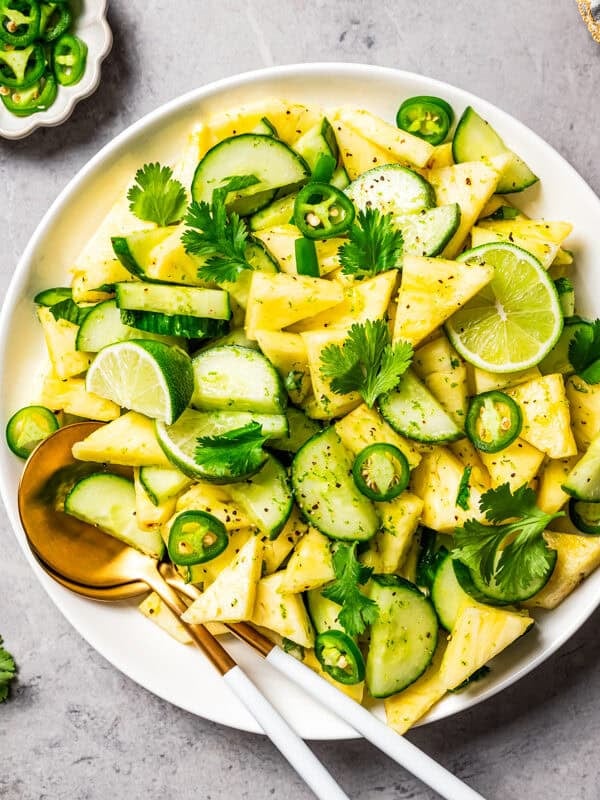 Pineapple cucumber salad served in a bowl, garnished with fresh cilantro and lime wedges.