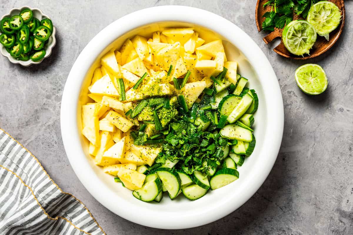 Chopped pineapple, cucumber, and cilantro in a white bowl.