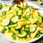 Cubed pineapples and cucumber slices in a salad bowl, garnished with lime and cilantro.
