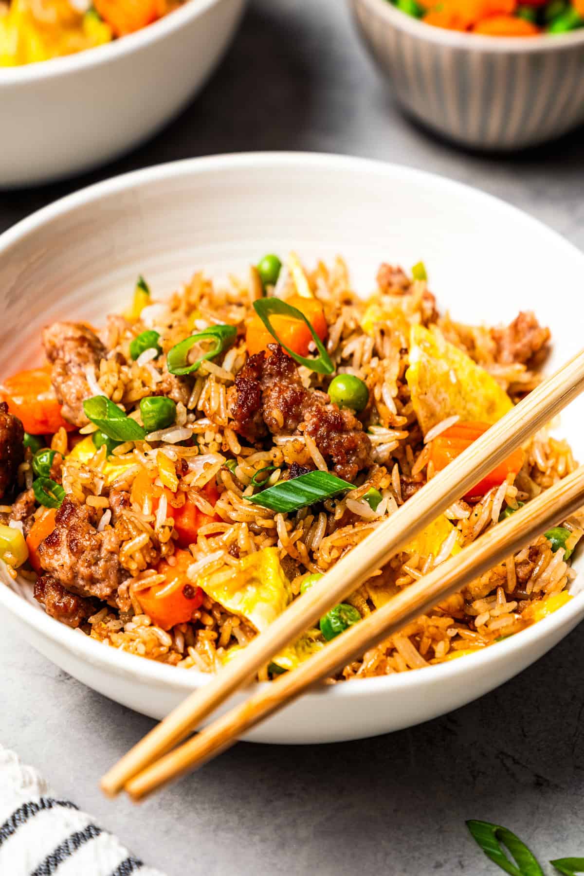 Pork fried rice is a quick, one-pan dinner packed with crispy ground pork, cooked eggs, and veggies. It's the best way to use up day-old rice! Pork fried rice served in a bowl with a set of chopsticks on the side.