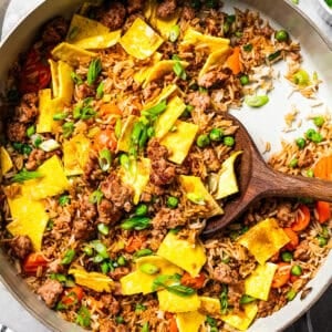 A wooden spoon resting in pork fried rice in a skillet.