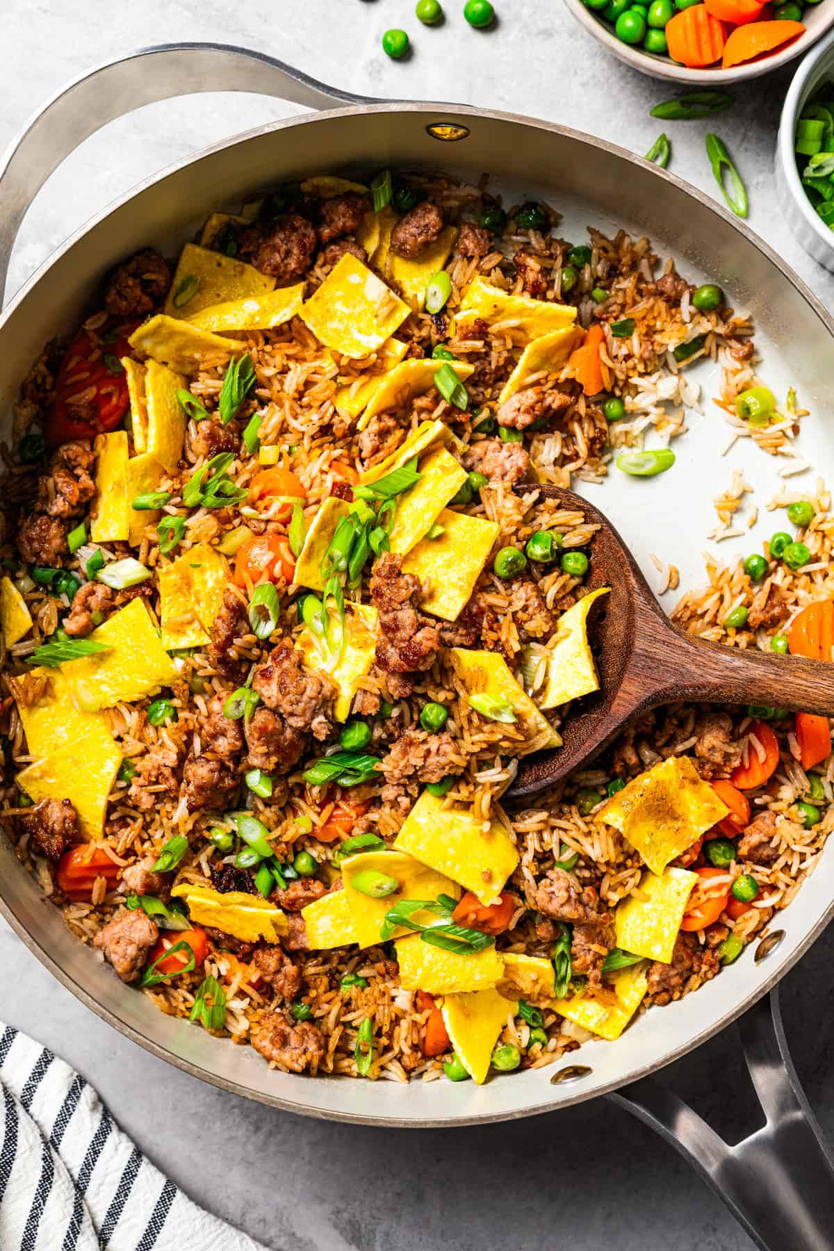 Pork fried rice is a quick, one-pan dinner packed with crispy ground pork, cooked eggs, and veggies. It's the best way to use up day-old rice! A wooden spoon resting in pork fried rice in a skillet.