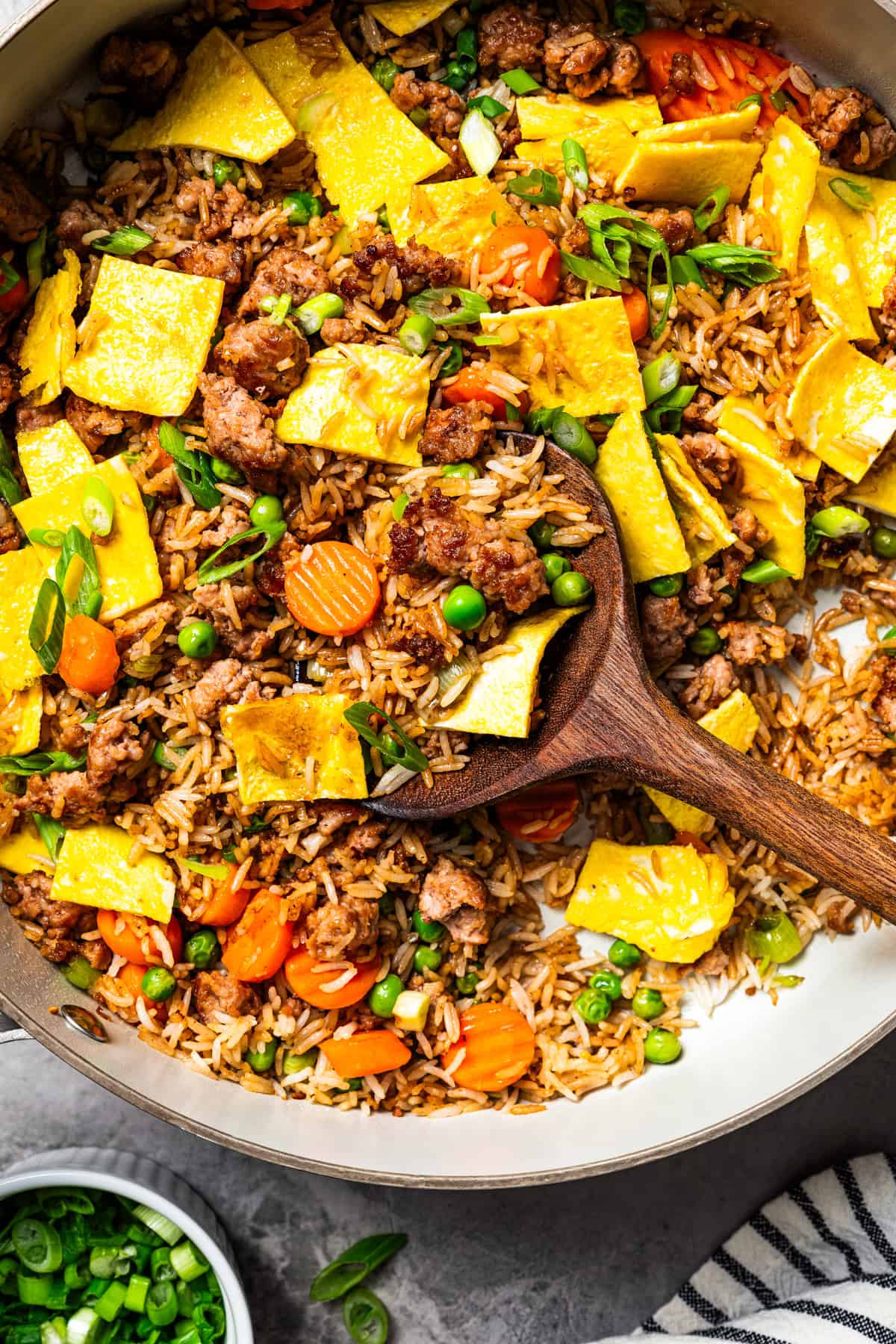 Pork fried rice is a quick, one-pan dinner packed with crispy ground pork, cooked eggs, and veggies. It's the best way to use up day-old rice! A wooden spoon resting in pork fried rice in a skillet.