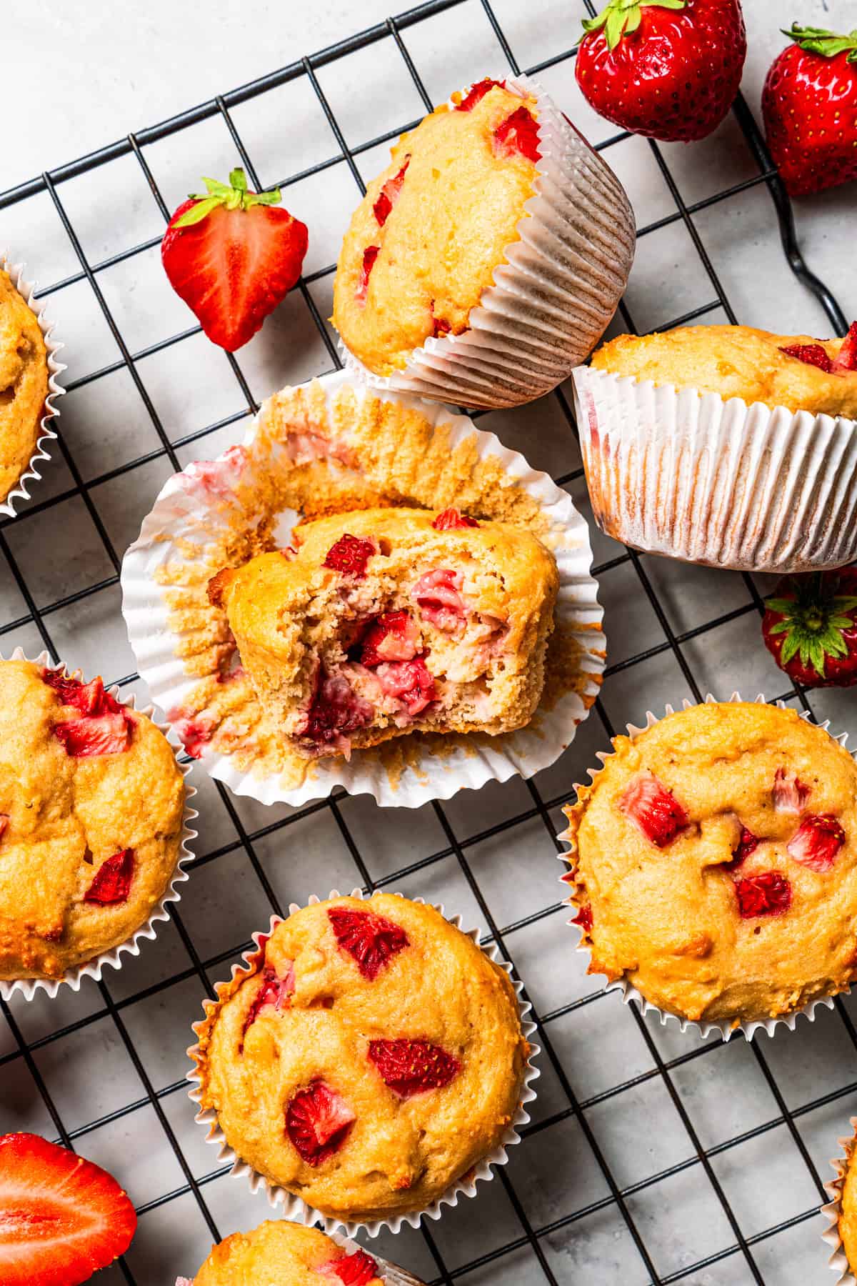 These moist strawberry protein muffins with applesauce, cottage cheese, and protein powder make an easy, light breakfast or meal prep snack! Moist strawberry protein muffins arranged on a wire rack, with a bite missing from the muffin in the center.