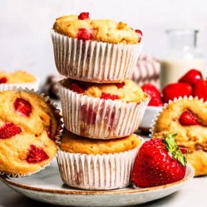 Three strawberry protein muffins stacked on a plate.