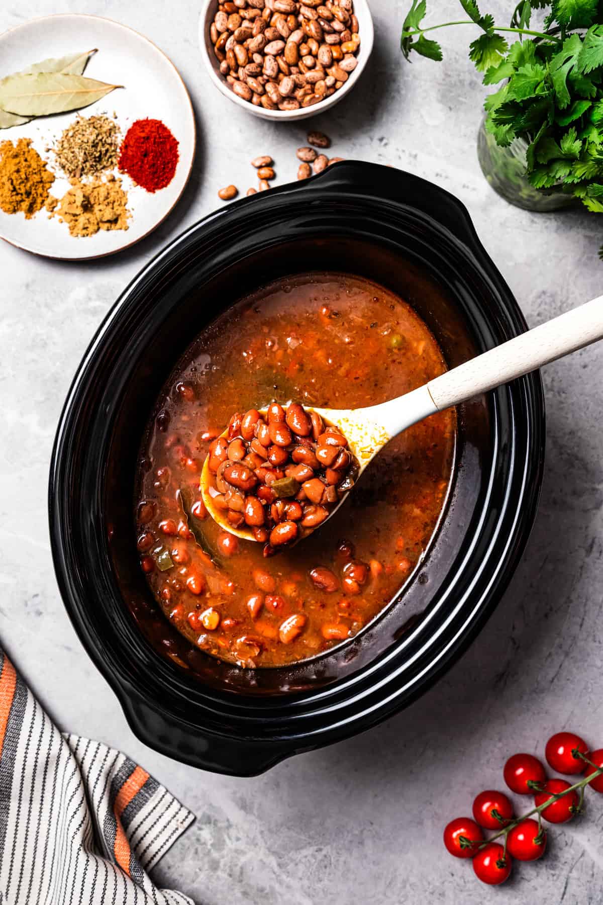 Slow cooker pinto beans are full of flavor and so easy to make. Add dry beans to the crock pot in the morning, and they’re tender by dinner! A spoon scooping out pinto beans from the slow cooker.