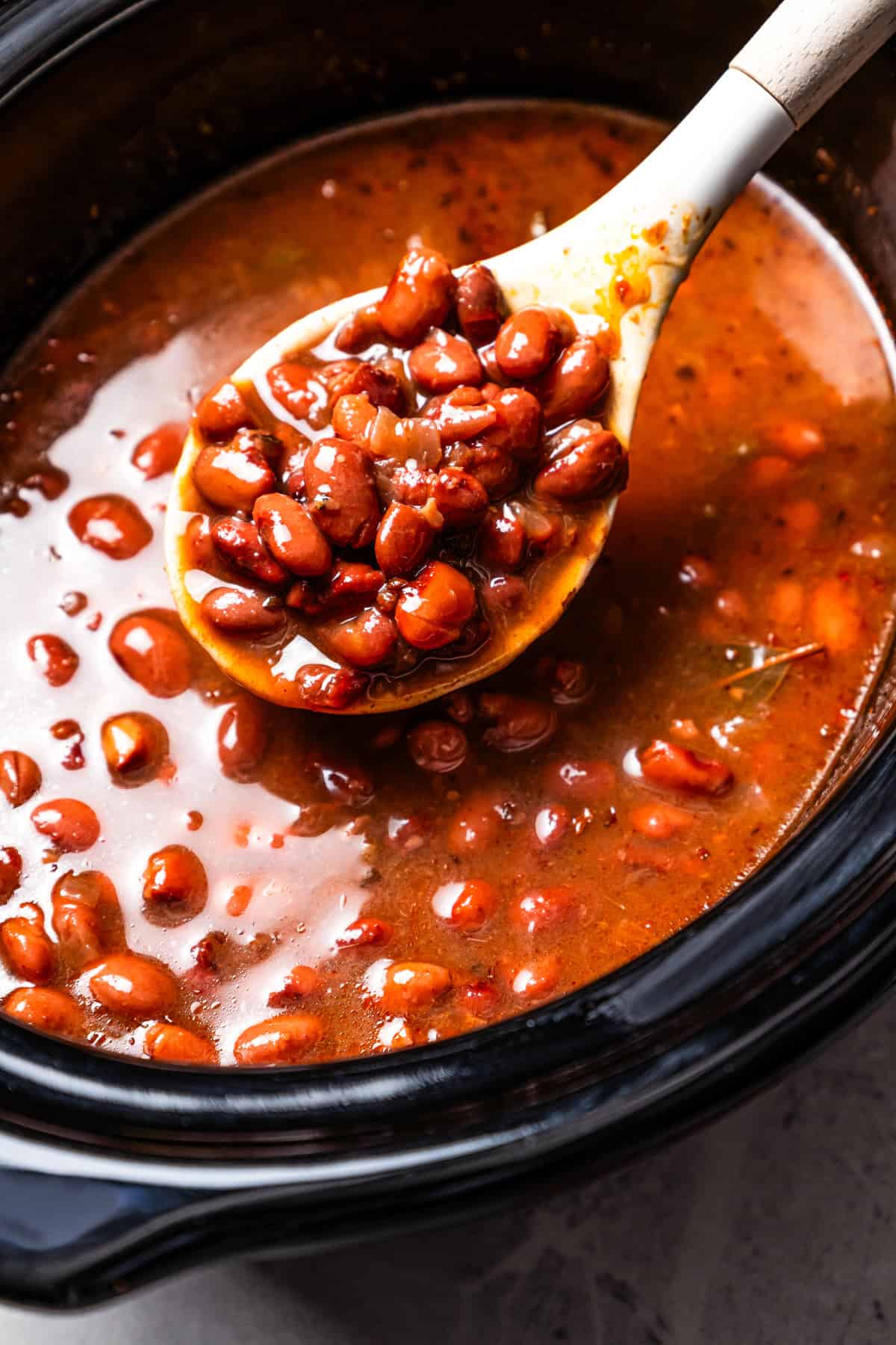 Slow cooker pinto beans are full of flavor and so easy to make. Add dry beans to the crock pot in the morning, and they’re tender by dinner! A spoon scooping pinto beans from the slow cooker.